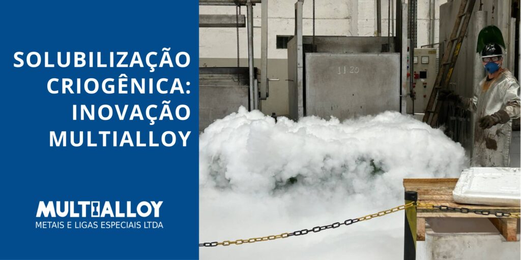 Fotografia industrial em plano médio mostrando o processo de solubilização criogênica na Multialloy. À esquerda, uma nuvem densa de vapor branco (nitrogênio líquido) cobre os componentes metálicos. À direita, um operador devidamente paramentado com EPIs aluminizados de proteção térmica observa o processo. O banner inclui o logotipo da Multialloy e o título 'Solubilização Criogênica: Inovação Multialloy'.